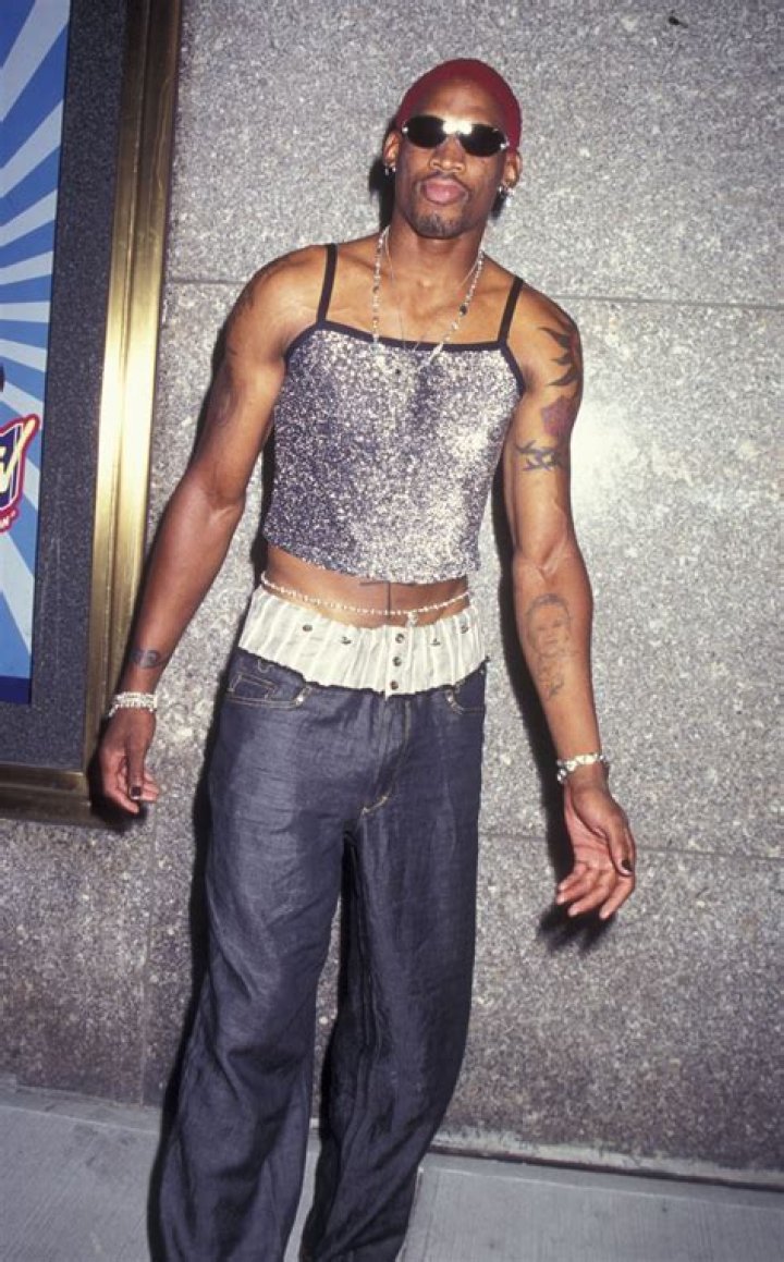 Dennis Rodman is wearing a cowboy hat, shades, and a black leather jacket as Annie Bakes is standing with him.